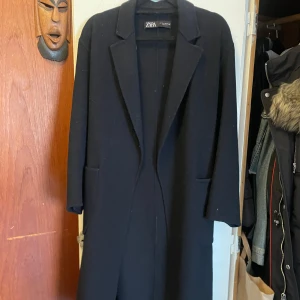 Marinblå kappa från Zara - Stilren marinblå kappa från Zara med klassisk krage och raka linjer. Lång modell med två stora fickor framtill och snöre runt midjan. Enkel design som passar till många outfits. Perfekt för dig som gillar minimalistisk stil.