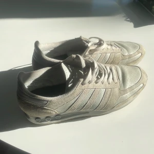 Adidas La Trainers - Snygga beige sneakers från Adidas med klassiska tre ränder på sidan. Skorna har ovandel i mocka och textil, snörning och platt sula med coola detaljer på sidan. Perfekta för dig som gillar en clean och sportig stil. De är använda, och har lite slitage men inget som märks. Passar 45-46