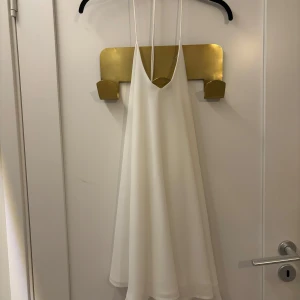 Vit kortklänning  - Vit kortklänning som har en öppen rygg med tunna band. Den hänger löst på kroppen och säljs då jag inte kan använda klänning utan bh.