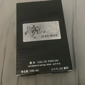 Jean Miss Eau de Parfum 100ml - Jean Miss Eau de Parfum i en stilren svart och silverfärgad förpackning. Flaskan är genomskinlig med svart detaljerad etikett och svart lock. Volymen är 100 ml och designen har en modern känsla med en ikonisk ryttare på etiketten.