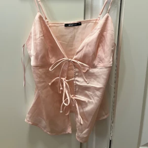 Ljusrosa jätte söt topp 💕💕 - Supersöt ljusrosa linnetopp från Gina Tricot med smala axelband och snygg snörning framtill. Toppen har v-ringning och är figurnära med en lätt glansig finish. Perfekt för att skapa en trendig och feminin look. Helt oandvänd men jätte snygg!!