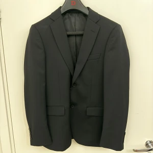 Svart kostym Dressmann slim fit 44 - Klassisk svart kostym från Dressmann i slim fit-modell. Byxorna är raka och matchar kavajen  (storlek 30/32). Använd vid 3 tillfällen, pris kan diskuteras vid snabb affär nu innan studenten. 