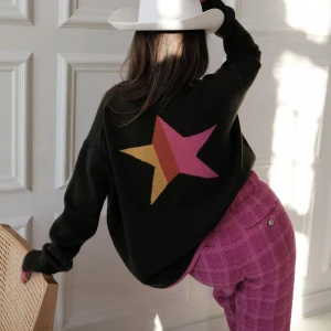 Chloe Shutterman City Sweater - Säljer en mörkgrön stickad tröja med färgglad stjärna i gult och rosa på ryggen. Tröjan har rund hals med rosa kant och texten 'Los Angeles' i rosa längs ena ärmen. Långärmad och loose fit – perfekt för dig som gillar statement-plagg. I bra skick! 🩷