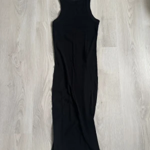 Svart långklänning i bomull - En stilren svart långklänning i mjuk bomull. Ärmlös modell med rund halsringning och figurnära passform. Perfekt för dig som gillar minimalistisk och clean stil.