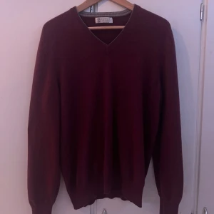 Vinröd kashmirtröja Brunello Cucinelli - Vinröd kashmirtröja från Brunello Cucinelli med v-ringning och långa ärmar. Tröjan har en klassisk, stilren look och är supermjuk tack vare det exklusiva kashmir-materialet. Perfekt för dig som gillar premiumkänsla och enkel design.