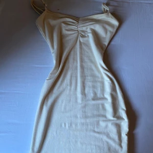 Ljusbeige tight klänning Oh Polly - Supersnygg ljusbeige klänning från Oh Polly med smala axelband och rynkdetalj vid bysten. Tight passform som framhäver figuren och mjukt stretchigt material. Perfekt för dig som gillar minimalistisk och stilren look.