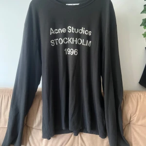  Acne Studios 1996 Longsleeve - Svart långärmad tröja från Acne Studios med tryck 'Acne Studios Stockholm 1996' på bröstet. Tröjan är i mjuk bomullsblandning med 15% hampa, har rund hals och en relaxed passform. Perfekt för en clean och stilren look. Size L men sitter lite som en XL.