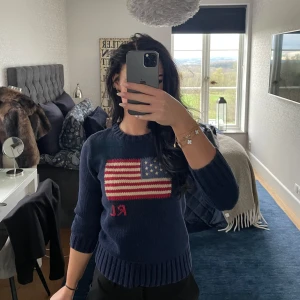 Mörkblå stickad tröja Polo Ralph Lauren iconic flag  - Obs! Gamla modellen, barnstorlek men passar som xs! Mörkblå stickad tröja från Polo Ralph Lauren med amerikansk flagga och RL-broderi framtill. Tröjan har rund hals, ribbade muddar och lång ärm. ikonisk detalj.