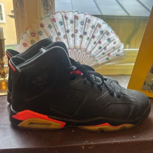 Nike Air Jordan 6 Retro svart/röd - Säljer ett par Nike Air Jordan 6 Retro i svart mocka med röda detaljer och genomskinlig sula. Klassisk high-top siluett med snörning och perforerade paneler. Perfekta för dig som vill sticka ut med en ikonisk sneaker.