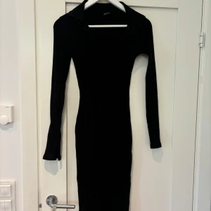 Svart ribbad långklänning Gina Tricot - Snygg svart klänning från Gina Tricot med ribbad struktur och lång ärm. Klänningen har krage och v-ringning. Perfekt för dig som gillar en tight passform och klassisk stil.