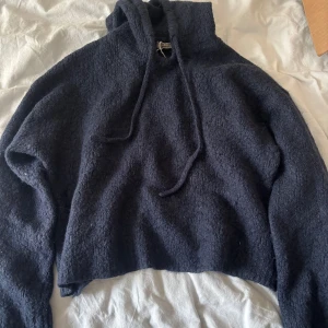 Mörkblå stickad hoodie från Gina Tricot - Mysig mörkblå hoodie från Gina Tricot i stickat material. Tröjan har huva med snörning och lång ärm, perfekt för kyliga dagar. Oversized passform för en avslappnad vibe. Snygg struktur i tyget som ger en cool look.