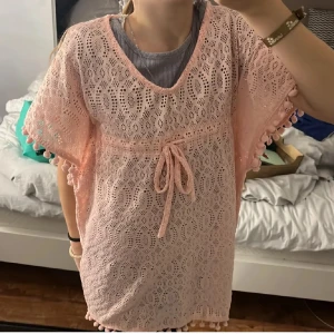 Söt ljusrosa spetsklänning med knyt - Superfin ljusrosa kortklänning i spets med knyt i midjan och söta bollar längs ärmar och nederkant. Klänningen har v-ringning och är kortärmad, perfekt för sommarens varma dagar. Den är loose fit och riktigt gullig till både sneakers och sandaler.