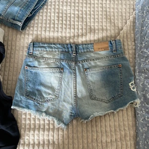 Blå jeansshorts med spets från g perfect jeans - Snygga blå jeansshorts från Gina tricot, jeans i storlek 34. De har fransig kant, slitningar och en stor vit spetsapplikation med blommor på ena sidan framtill. Klassisk femficksmodell med knapp och dragkedja. Perfekta för sommaren!❤️