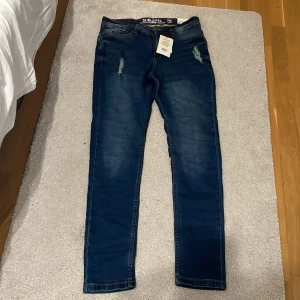 Mörkblå jeans Sublevel W29 L32 - Snygga mörkblå jeans från Sublevel med slitna detaljer framtill. Klassisk femficksmodell med orange kontrastsömmar och dragkedja. Jeansen har en väldigt bra passform.