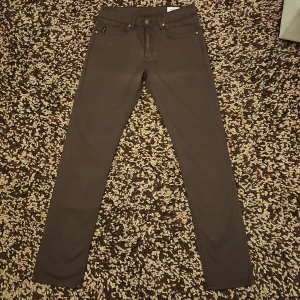 Bruna skinny jeans från Armani - Snygga bruna jeans från Armani med klassisk femficksdesign och guldfärgade detaljer. Byxorna har skinny passform och är tillverkade i bomullsmix för en bekväm känsla. Bakfickan har den ikoniska Armani-loggan i guld. Perfekta för dig som gillar stilrena och smala jeans.