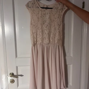 Ljus spetsklänning från Vila - Supersöt ljus kortklänning från Vila med spets upptill och flowy kjol. Klänningen har öppen rygg med knapp i nacken och dragkedja i sidan. Perfekt för sommarens alla tillfällen! Färgen är ljusbeige och materialet känns lätt och luftigt.