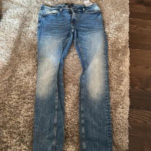 Blå raka jeans med slitningar - Snygga blå jeans med raka ben och slitna detaljer på både fram- och baksida. Klassisk femficksmodell med dragkedja och knapp i midjan. Jeansen har en cool tvättad look och passar perfekt till en avslappnad stil.
