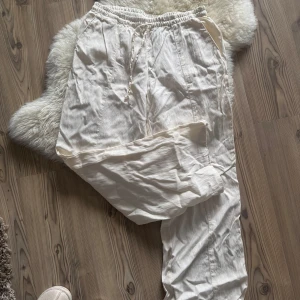 Vita linnebyxor med snörning - Säljer ett par vita linnebyxor med avslappnad passform och resår i midjan. Byxorna har snörning framtill, raka ben och praktiska fickor både fram och bak. Perfekta för varma dagar och ger en chill vibe.