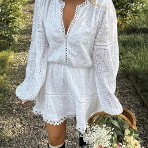Vit klänning/studentklänning - Superfin vit kort klänning med broderade hål, v-ringning och långa puffiga ärmar. Klänningen har volangkant nertill och markerad midja. Helt slutsåld och oanvänd!! Lappen kvar.