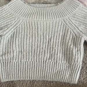 Ljusgrå stickad tröja från Divided - Supermysig ljusgrå stickad tröja från Divided, H&M. Tröjan har en chunky ribbstickad struktur, bredare halsringning och är croppad i modellen. Perfekt att styla med höga jeans eller kjol för en chill look.
