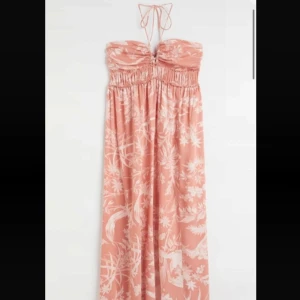Persikofärgad långklänning  - Supersöt långklänning i persikofärg med vitt blommigt mönster. Klänningen har halterneck med knyt och är axelbandslös. Aldrig använd därmed är prislappen kvar!💕💕