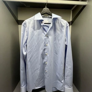 Ljusblå slim fit skjorta från Eton - Snygg ljusblå skjorta från Eton i slim fit-modell. Skjortan har klassisk krage, långa ärmar och knäppning framtill med vita knappar. Perfekt för dig som gillar stilrena och fräscha plagg. Tillverkad i mjuk bomull för en skön känsla hela dagen.