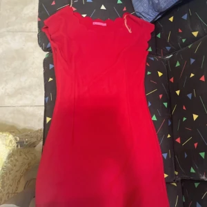 Röd kortklänning - Snygg röd kortklänning med vågad kant vid urringningen och korta ärmar. Klänningen har en figurnära passform och är perfekt för dig som vill sticka ut. Enkel men ändå unik design som passar till många tillfällen.