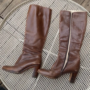 Bruna italienska skinnstövlar med klack - Snygga bruna stövlar i äkta skinn, tillverkade i Italien. Modellen har en rund tå, dragkedja på insidan och en stabil klack. Perfekta för dig som gillar klassisk stil med en touch av vintage. Skorna är i storlek 38 och har en tidlös look. Är använda och pris kan diskuteras!