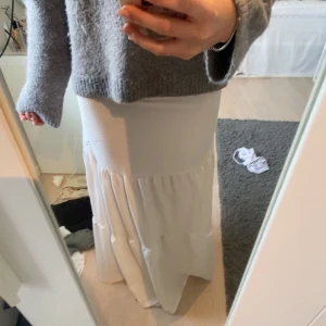 Vit långkjol med volang - Säljer en vit långkjol med volangdetaljer. Kjolen har en rak passform upptill och faller snyggt ner mot golvet med en lätt rynkad volang nedtill. Perfekt för en fräsch och stilren look.