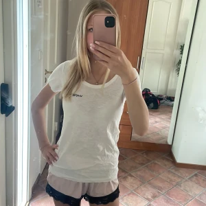 Vit t-shirt Wellness Studio - Vit t-shirt från Wellness Studio med svart tryck fram och bak. Klassisk rund halsringning och korta ärmar. Skön och enkel modell i bomull, perfekt till träning eller chill. Sitter snyggt och har en clean look.