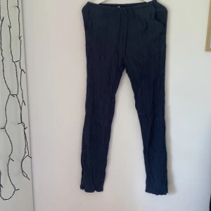 Mörkblå crinklebyxor från Zara - Snygga mörkblå byxor från Zara i crinklat tyg. De har elastisk midja med snörning och raka ben. Perfekta för en chill och stilren look. Lätta och luftiga, passar bra till både sneakers och sandaler.