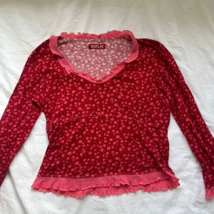 Blommig tröja - Supersöt långärmad tröja från Replay i rött med små rosa blommor. V-ringad med volangkant i rosa vid halsringning och nederkant.