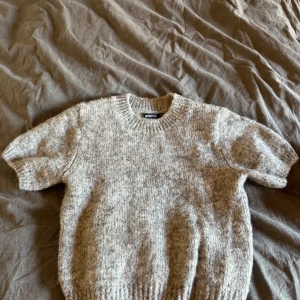 Grå stickad kortärmad tröja Gina Tricot - Mysig grå stickad tröja från Gina Tricot med korta ärmar och rund halsringning. Tröjan har en ribbad kant vid hals, ärmslut och nederkant. Perfekt för lager-på-lager och chill vibes under höst och vinter. Använd fåtal gånger. Skriv om man vill ha bild på