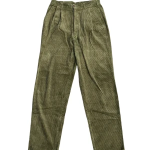 Olivgröna manchesterbyxor SAAF - Olivgröna manchesterbyxor från SAAF med klassisk rak passform och hög midja. Byxorna har tydliga ribbor, bakfickor med knappar och bälteshällor. Perfekta för dig som gillar retrovibbar och vill sticka ut med en cool färg och struktur.