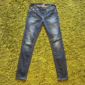 True Religion skinny jeans blå, stl 27 - Säljer ett par klassiska blå skinny jeans från True Religion i storlek 27. Jeansen har snygga kontrastsömmar, ikoniska bakfickor med lock och silverfärgade knappar. Modellen är tight och har låg midja. Perfekta för dig som gillar en slimmad look.