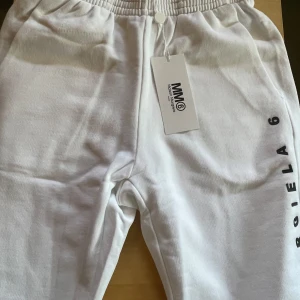 Vita mjukisbyxor Maison Margiela MM6 - Snygga vita mjukisbyxor från Maison Margiela MM6 med svart logotyp längs benet. Perfekta för en chill och trendig look. Går ner till början av knäna. Helt nya shorts köptes för lite mer än dubbelt av priset.