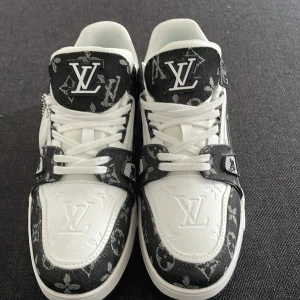 Louis Vuitton svartvita sneakers - Exklusiva Louis Vuitton sneakers i svart och vitt med tydlig LV-logga och monogrammönster. Skorna har snörning, platt sula och detaljer i präglat skinn samt textil. Snygg kontrast mellan svart och vitt, med klassiska LV-detaljer på både ovandel och sula.