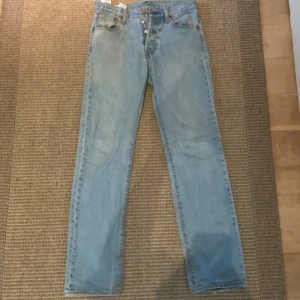 Levi's 501 ljusblå jeans straight fit - Klassiska Levi's 501 jeans i ljusblå denim med raka ben och hög midja. Jeansen har fem fickor, knappgylf och den ikoniska läderpatchen bak. Använts helt ok mycket och syns att de är inte sprillansnya men dem ser forfarande väldigt bra ut. Storlek 29x32
