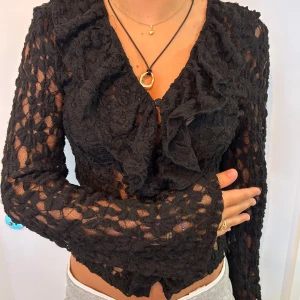 Svart spetsblus med volang från Vero Moda - Supersnygg svart långärmad spetsblus från Vero Moda med v-ringning och volangdetaljer framtill. Blusen är transparent med blommigt mönster och har en figurnära passform. Funkar både på fest samt formella sammanhang. Priset är diskuterbart. Köpte för 500 men säljer för 300kr trots helt oanvänd. Säljer för att jag har tappat bort kvittot. 