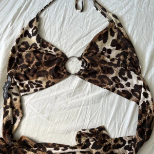 Leopardmönstrad omlottopp PrettyLittleThing - Säljer en leopardmönstrad omlottopp från PrettyLittleThing med knyt i nacken samt ryggen och snygg ringdetalj framtill. Toppen är ärmlös och har croppad passform, perfekt för att sticka ut. Materialet är mjukt och bekvämt. Vid frågor hör av dig!