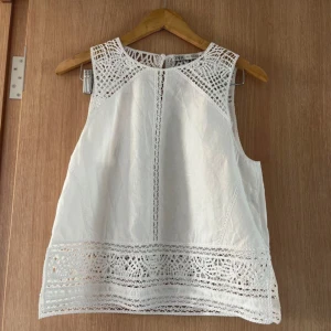 Llinnetopp Zara - Superfin vit linnetopp från Zara med snygga virkade spetsdetaljer upptill och nedtill. Ärmlös modell med rund halsringning och lätt A-linjeform. Perfekt för varma dagar och ger en fräsch och somrig vibe.