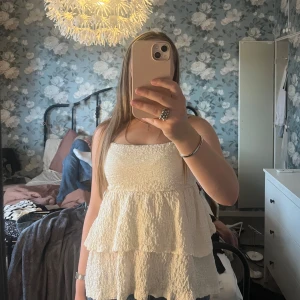 Benvit volangtop från Gina Tricot - Supersöt benvit topp från Gina Tricot med smala axelband och volanger. Toppen har en crinklad struktur och är lätt utsvängd nertill för en flowy känsla. Perfekt för varma dagar när du vill ha något luftigt och stilrent.