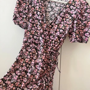 Blommig klänning  - Superfin kort omlottklänning med blommigt mönster i rosa, vit och svart. Tyvärr för liten för mig! 