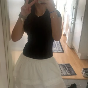 Vit volangkjol från BikBok - Vit kortkjol från BikBok med flera lager volanger och spetsdetaljer. Jag hade tjolen som lågmidjad i bilden men den är gjort för att vara lagom. Använt kanske 4-5 gånger. 