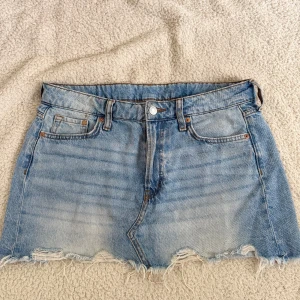 Blå jeanskjol - Säljer en blå jeanskjol från H&M med fransig nederkant och klassiska fickor fram och bak. Kjolen är i storlek S men är stor i storleken.🩵