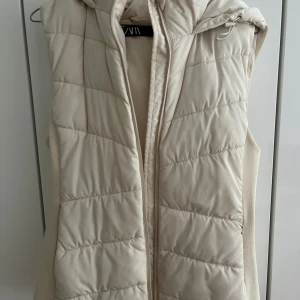 Mysig dunväst med huva - En supermysig vit/beige dunväst från Zara. Perfekt för en kylig höstdag. Västen har en vacker huva och ribbade sidor som gör den extra bekväm. Perfekt för lager-på-lager och en clean look. Kan användas för flera olika tillfällen! 