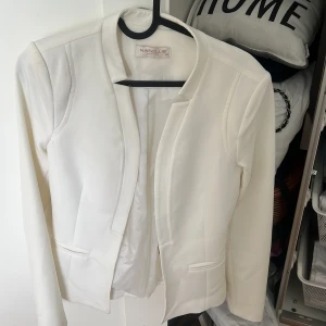 Vit kavaj från Nasello, storlek 36 - Snygg vit kavaj från Nasello i klassisk modell med lång ärm och raka linjer. Kavajen har två fickor framtill och är helfodrad för en clean look. Perfekt att slänga över en topp för en stilren outfit.
