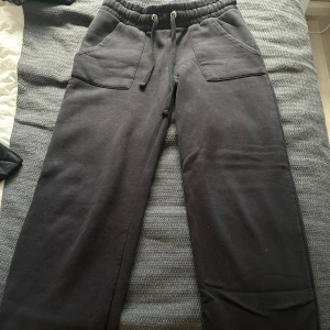 Svarta mjukisbyxor med snörning - Svarta mjukisbyxor med elastisk midja och snörning framtill. Byxorna har två stora fickor fram och två bakfickor. De är raka i modellen.