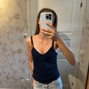 Mörkblå linnetopp från Romwe  - Säljer en mörkblå linnetopp från Romwe i storlek XS. Toppen har smala axelband, v-ringning och diskret broderad blomdetalj framtill. Materialet är lätt och stretchigt, perfekt för varma dagar. Snyggt vågig nederkant för extra detalj.