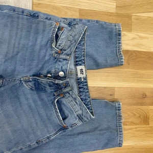  ljusblå jeans straight fit - Ljusblå Levis 501 jeans med klassisk straight mid waist. Jeansen har knäppning med knappar, fem fickor och råa benslut för en avslappnad vibe. Tillverkade i slitstarkt bomullsjeans som ger en tidlös look.